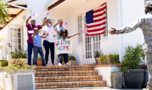 military veteran comes home to family waving small American Flags and signage welcome home American VA Loans
