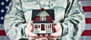 Man in military uniform holds small house in his hands American VA Loans